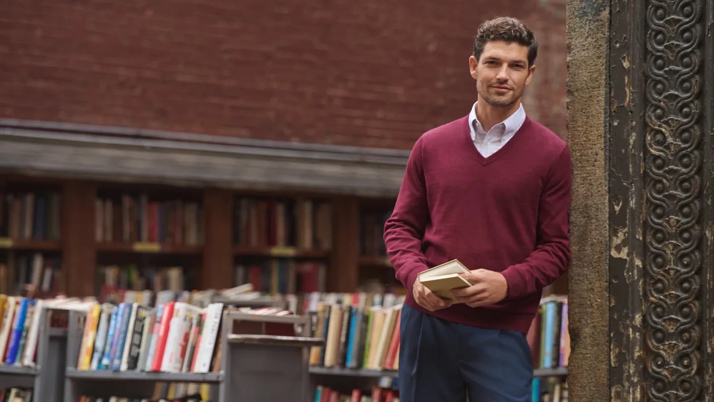 Man wearing seasonal staples from Men's Wearhouse in front of bookshelves
