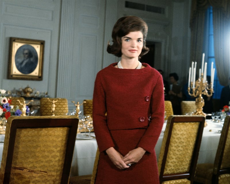 American First Lady Jacqueline Kennedy (1929 - 1994), in a red dress, stands in before a dining room table in the White House during the filming of a CBS News Special program called 'A Tour of the White House with Mrs. John F. Kennedy,' Washington DC, January 15, 1962. (Photo by CBS Photo Archive/Getty Images)