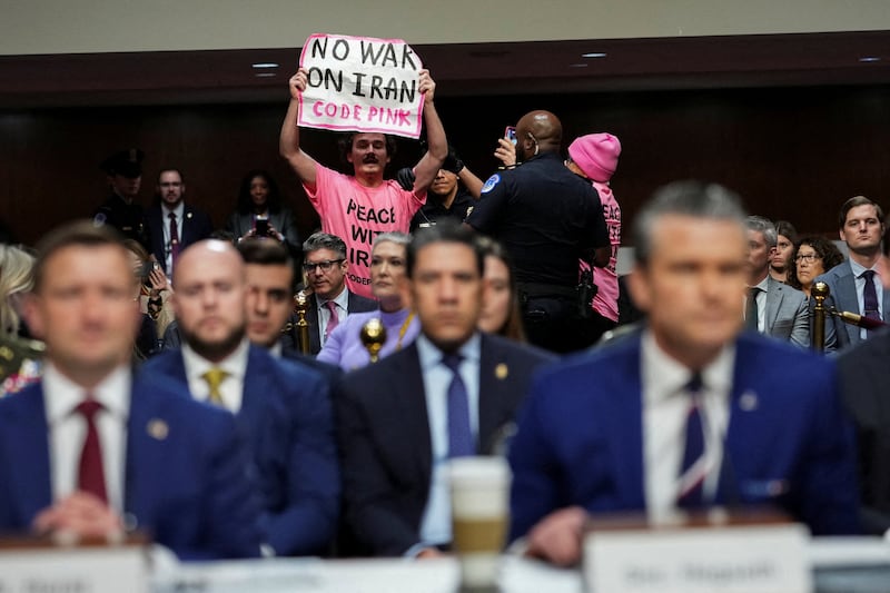 A protester holds a banner opposing the war with Iran.