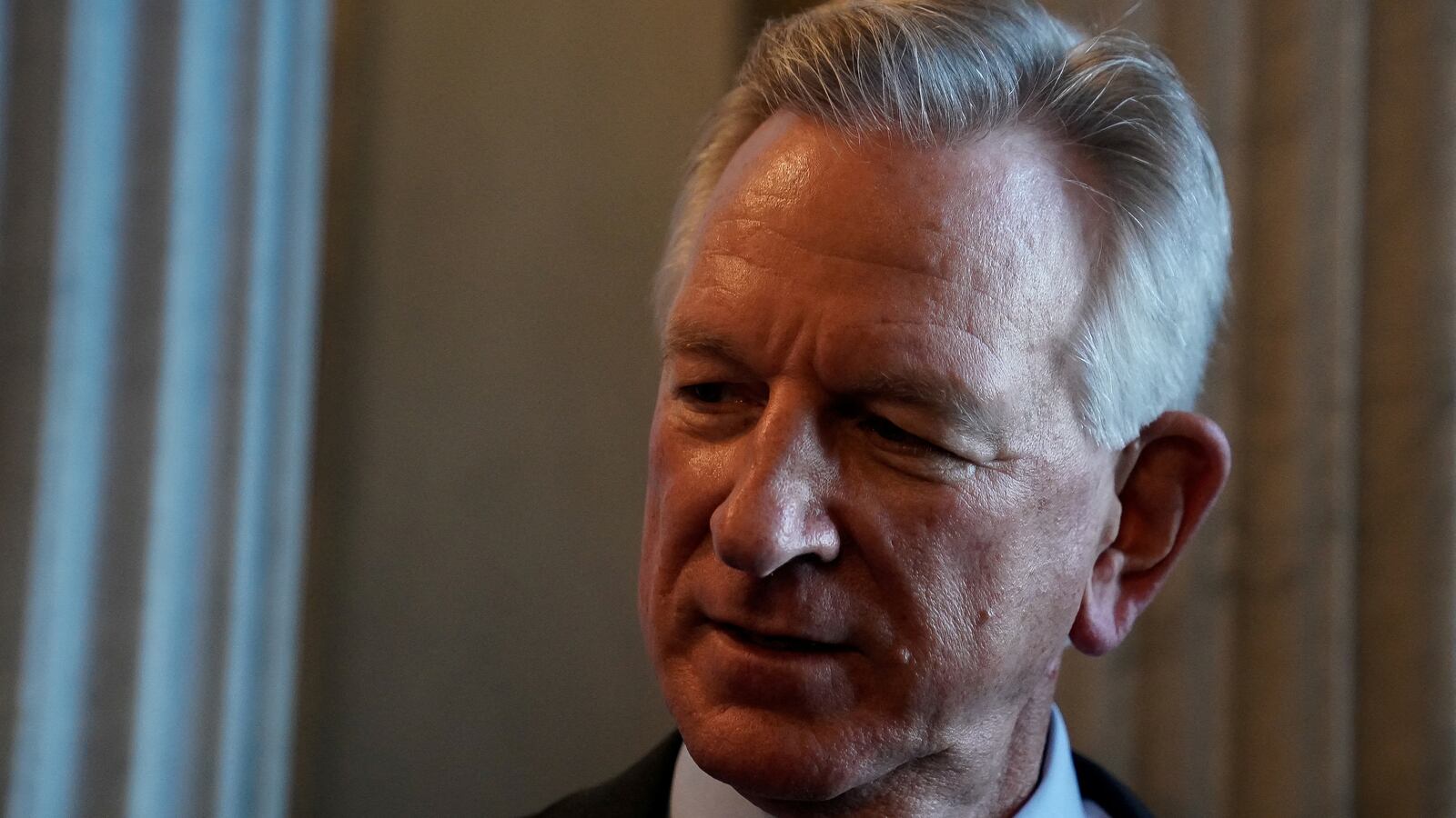 Tommy Tuberville speaks to reporters in a dimly-lit room.