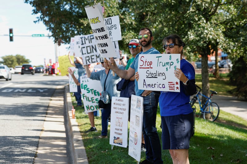 People hold signs during an anti-Trump protest as President Donald Trump attends the Presidents Cup golf tournament at Medinah Country Club in Medinah near Chicago, Illinois, September 27, 2026.