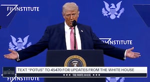 Donald Trump stands on stage at a lecture with his arms stretched out.