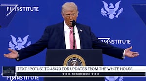 Donald Trump stands on stage at a lecture with his arms stretched out.