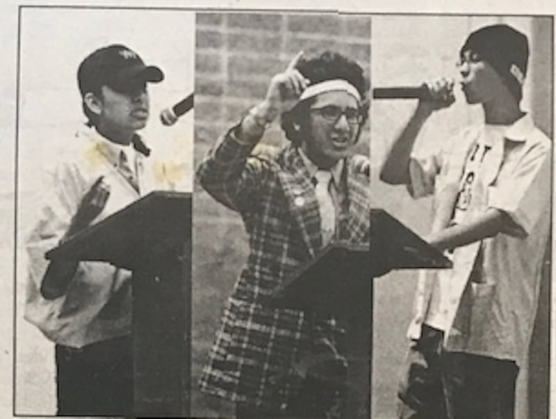 A black and white photo of three people speaking on a stage