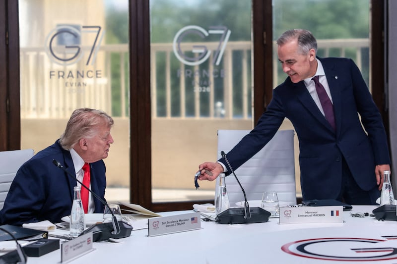 Carney shows a watch to Trump at a G7 summit in June. The two leaders have announced steep tariffs in the wake of a trade deal falling apart last Friday.