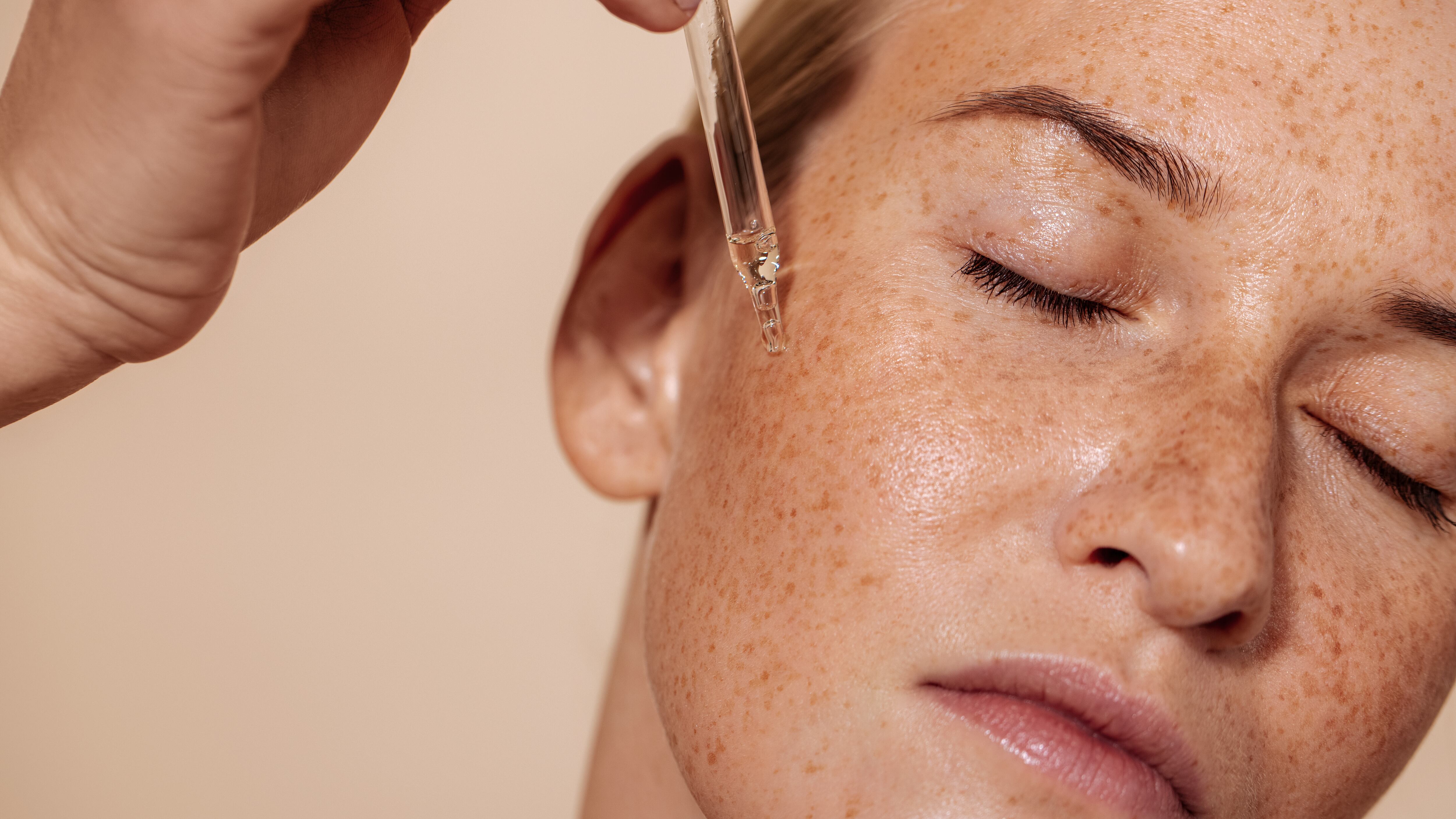 Young beautiful woman with closed eyes applying face serum with pipette