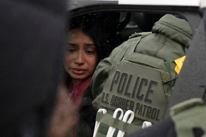 A detained woman sits inside a vehicle surrounded by ICE agents.