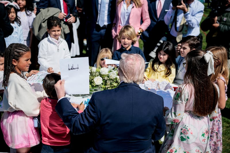 President Donald Trump holds a piece of paper with his signature as he sits among children during the 2026 White House Easter Egg Roll at the White House in Washington, D.C., U.S., April 6, 2026.
