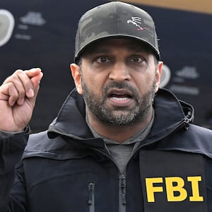 FBI Director Kash Patel stands at a lecture in between two law enforcement officials at a news conference.
