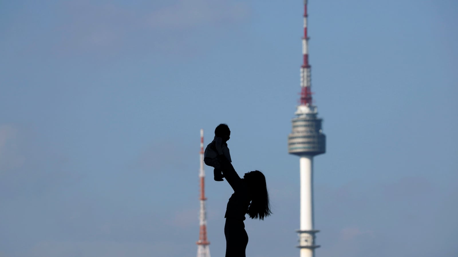 A woman holding up her baby is silhouetted against the backdrop of N Seoul Tower, commonly known as Namsan Tower, in Seoul, South Korea, October 2, 2018.
