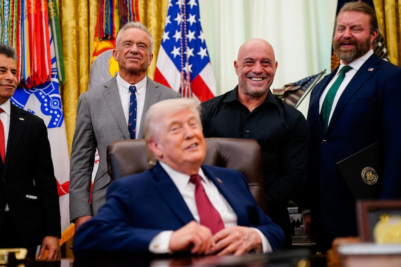 Americans for Ibogaine CEO Bryan Hubbard, podcaster Joe Rogan and U.S. Health and Human Services (HHS) Secretary Robert F. Kennedy Jr. stand behind President Donald Trump, after he signed an executive order about easing restrictions on mental health treatments, including, ibogaine, in the Oval Office of the White House in Washington, D.C., April 18, 2026. REUTERS/Nathan Howard