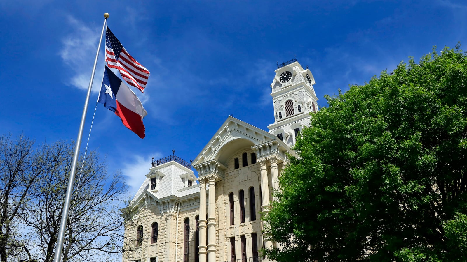 American and Texas flags fly in front of the Hill County courthouse in Hillsboro Texas.