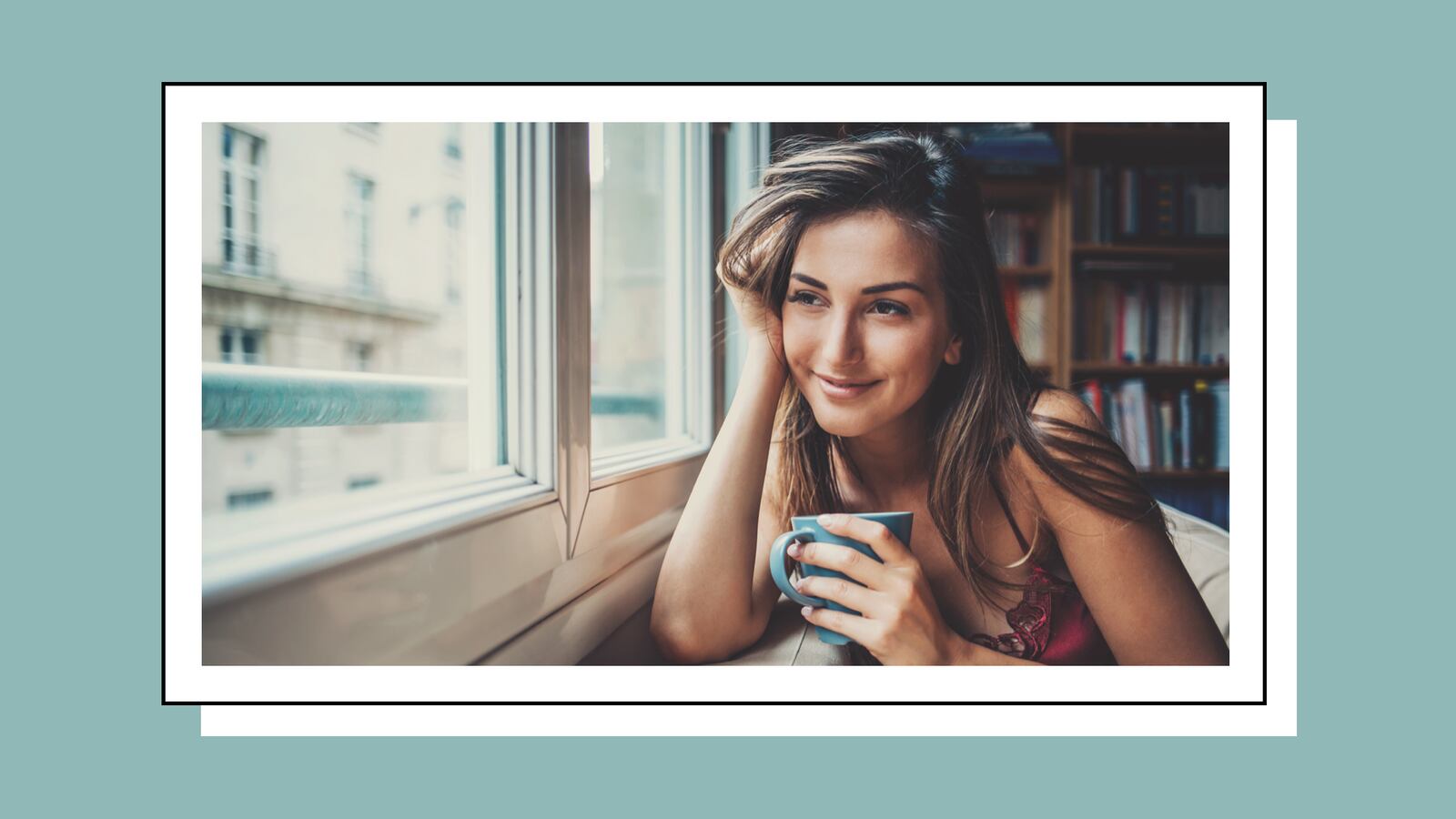 Woman in an apartment looking out the window while holding an aqua-colored mug.