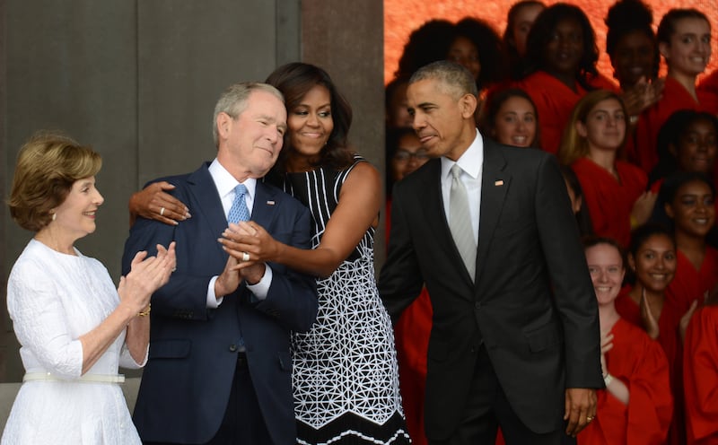 President Barack Obama watches First Lady Michelle Obama embracing former president George Bush, accompanied by his wife, former first lady Laura Bush, while participating in the dedication of the National Museum of African American History and Culture on September 24, 2016 in Washington, D.C.