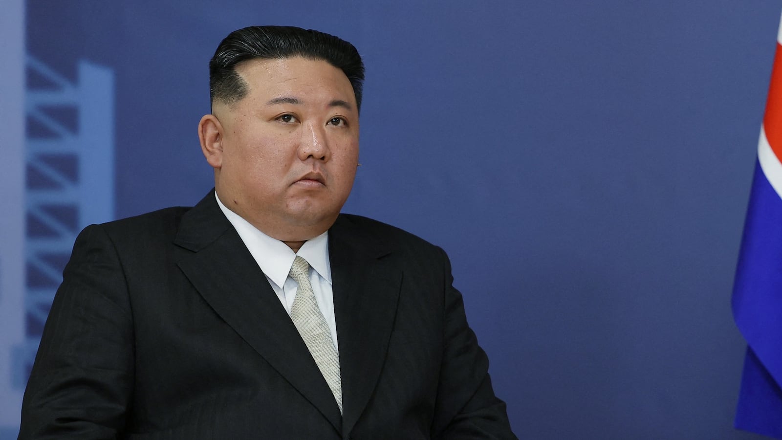 North Korean leader Kim Jong un sits next to a flag.