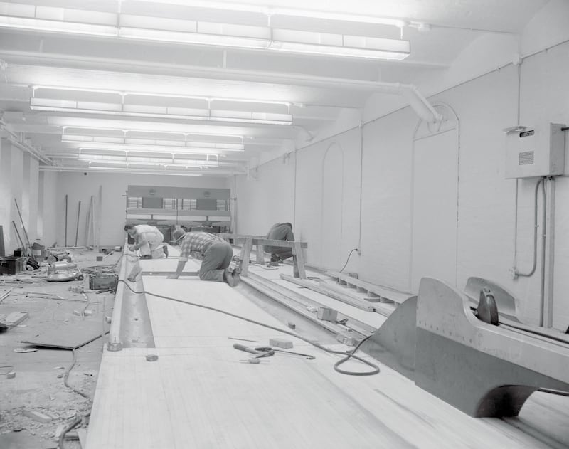 Feb 1955, White House Bowling Alleys Moved Across Street. Washington, D.C.: The bowling alleys installed in the White House while Harry Truman was president have been removed and are being set up in the basement of the old State Department building across the street from the presidential mansion. The $5,000 twin alleys were removed to make room for additional office space. Photo shows two workmen installing the alleys in their new location.