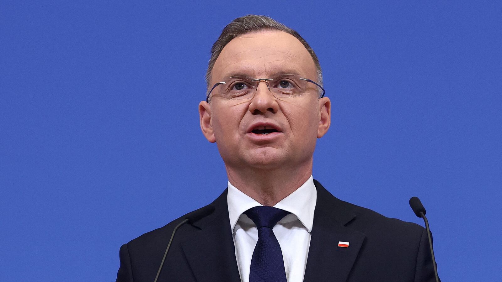 Polish President Andrzej Duda speaks before a blue background.