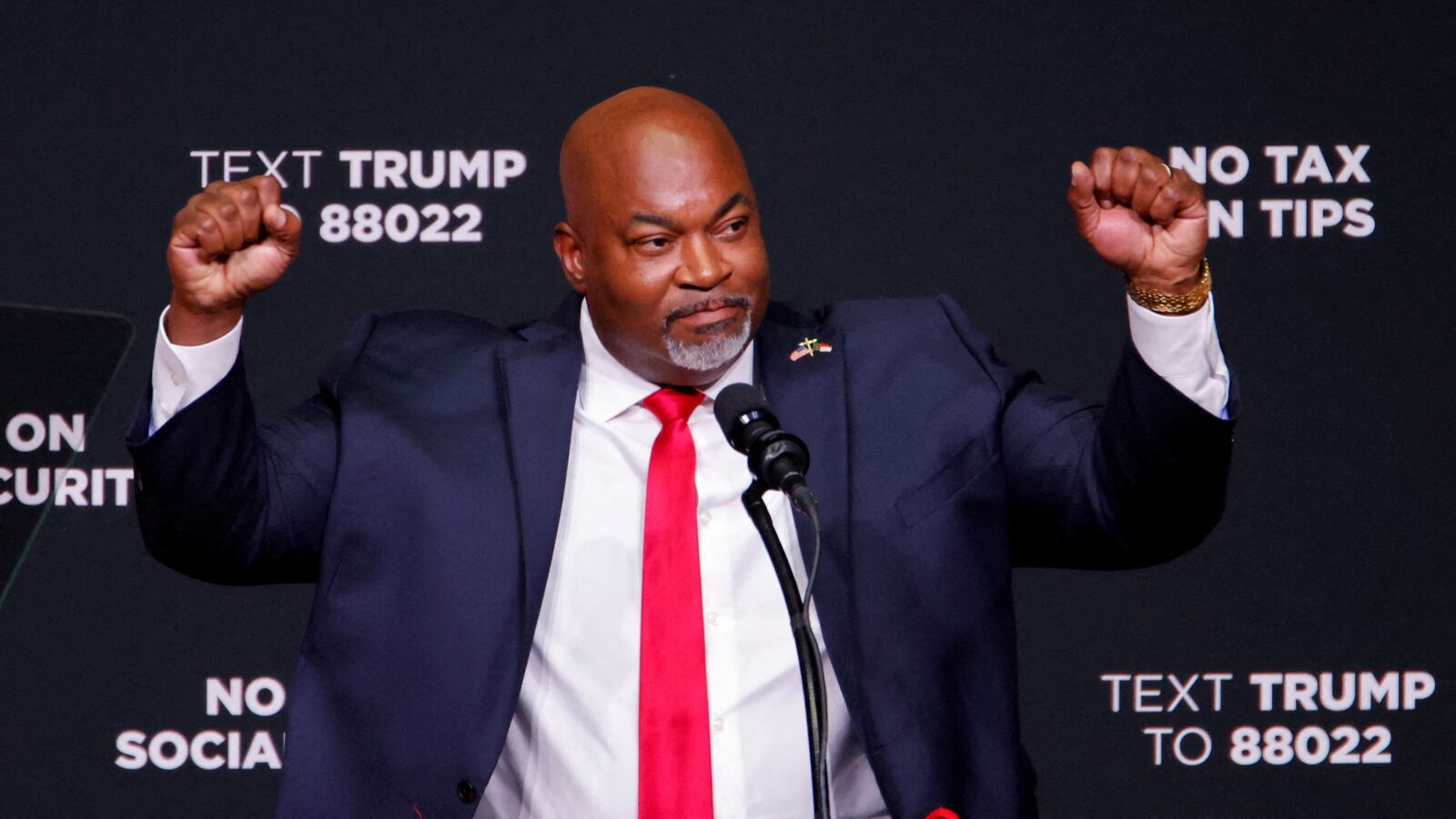 Mark Robinson raises his hands while standing behind a podium.