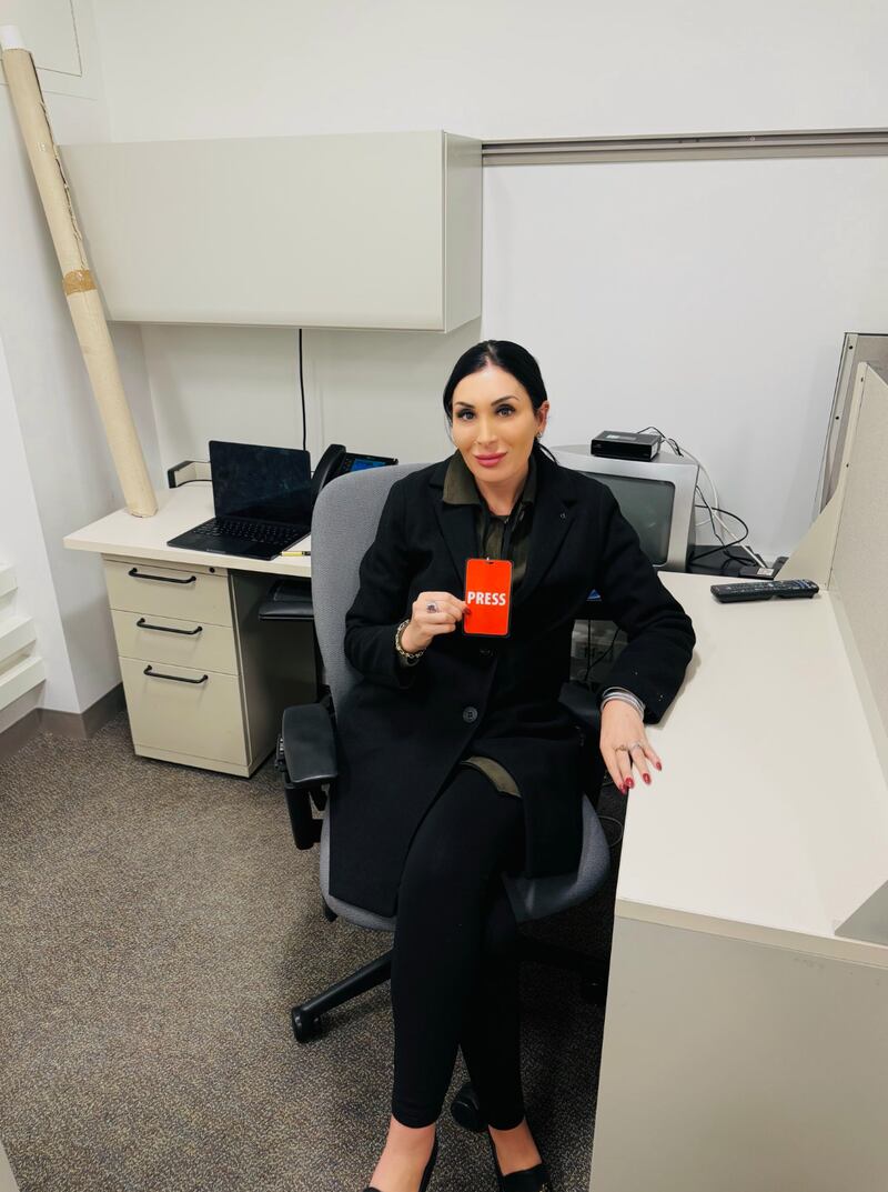 Laura Loomer sits at office desk holding a press pass.