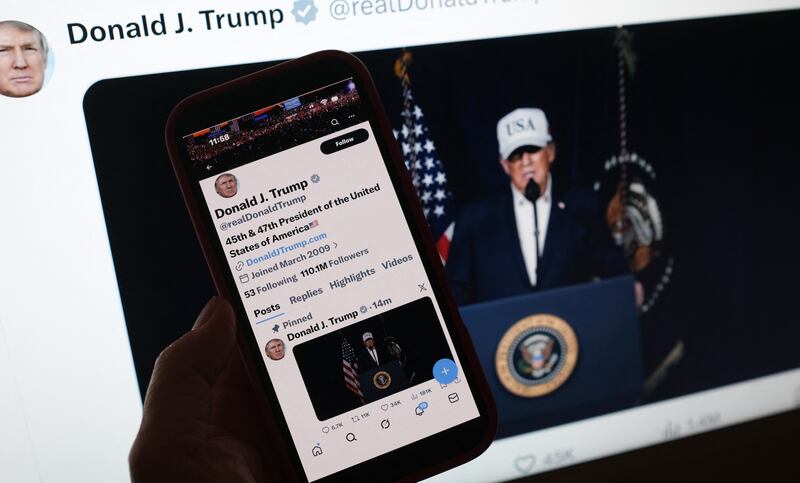 This illustration image shows a person looking at a smartphone displaying US President Donald Trump making a statement regarding combat operations on Iran, alongside a computer screen featuring the same message posted on X on February 28, 2026. US President Donald Trump announced February 28 that