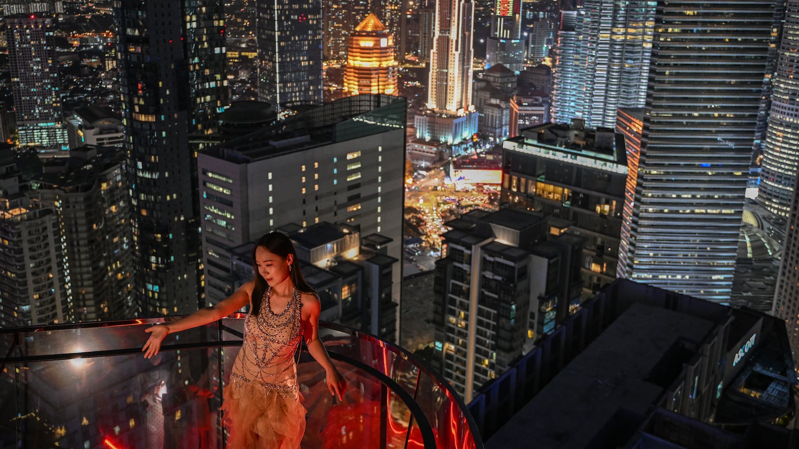 TOPSHOT - A woman poses for a photo with the night skyline in the background in Kuala Lumpur on May 29, 2025. (Photo by Jam STA ROSA / AFP) (Photo by JAM STA ROSA/AFP via Getty Images)