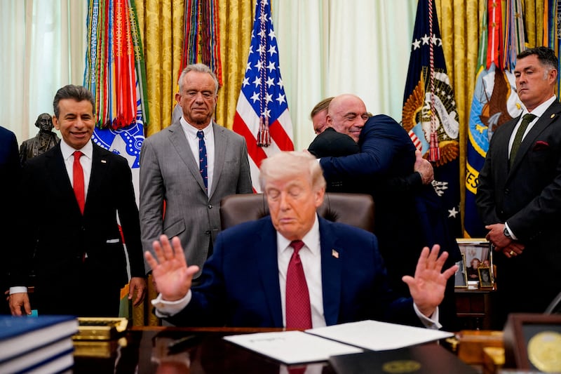 Americans for Ibogaine CEO W. Bryan Hubbard and podcaster Joe Rogan hug next to U.S. Health and Human Services (HHS) Secretary Robert F. Kennedy Jr., as U.S. President Donald Trump gestures after he signed an executive order about easing restrictions on mental health treatments, including, ibogaine, in the Oval Office of the White House in Washington, D.C., April 18, 2026. REUTERS/Nathan Howard REFILE - ADDS "W." TO "W. BRYAN HUBBARD".     TPX IMAGES OF THE DAY