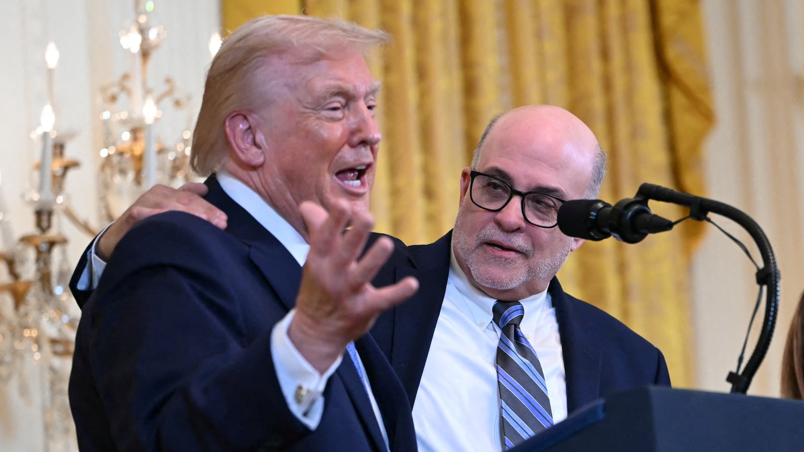 US President Donald Trump is joined on the podium by conservative radio host Mark Levin and his Julie Strauss Levin at a Hanukkah reception in the East Room of the White House in Washington, DC, on December 16, 2025. (Photo by ANDREW CABALLERO-REYNOLDS / AFP via Getty Images)