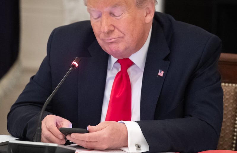 President Donald Trump using his cellphone at a table.