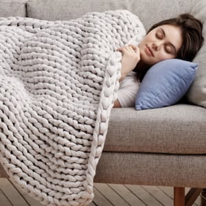 Woman sleeping on a couch with a Bearaby weighted blanket and light blue pilliow.