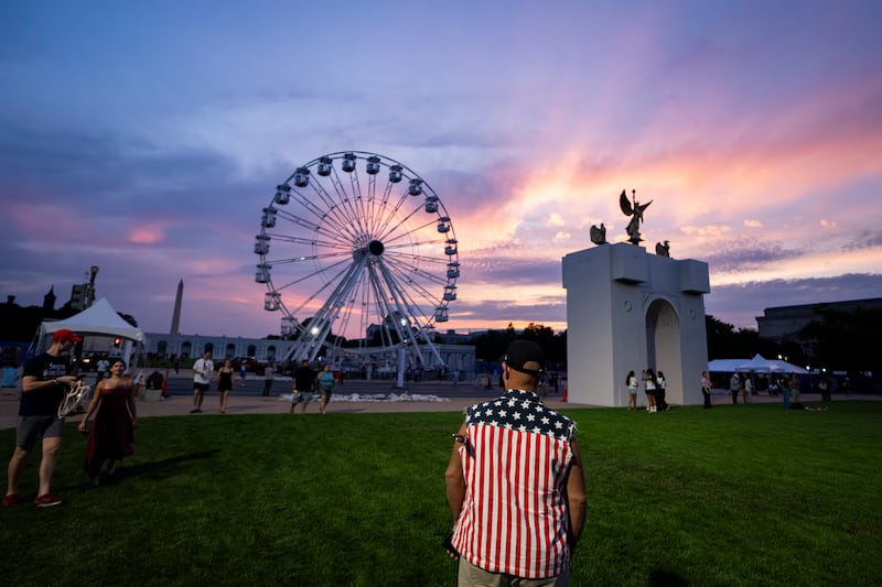 The sun sets behind a replica of the planned Triumphal Arch and the 110-foot "Freedom 250" ferris wheel on the first day of the Great American State Fair on the National Mall.