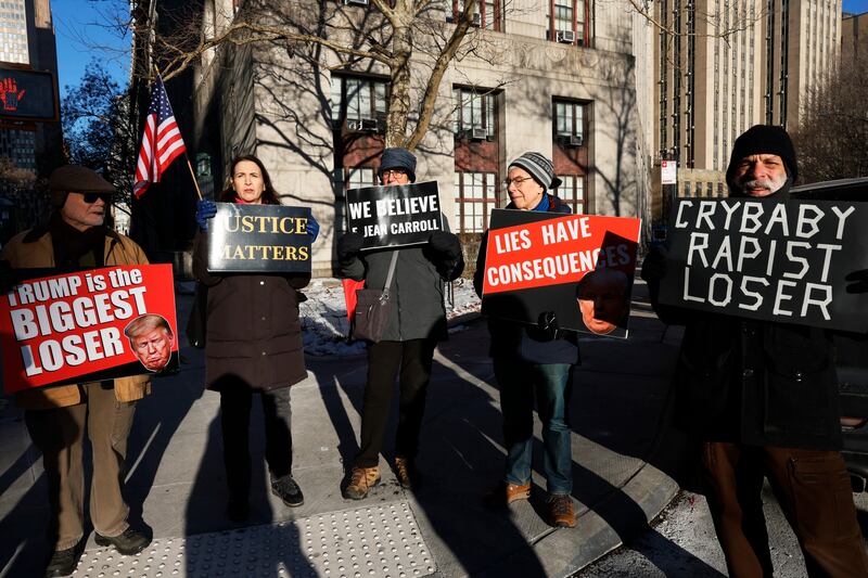 NEW YORK, NEW YORK - JANUARY 22: Protestors hold up signs outside of Manhattan Federal Court before the start of the E. Jean Carroll civil defamation trial against former President Donald Trump on January 22, 2024 in New York City. Former President Trump is scheduled to testify in his civil defamation trial on the eve of the New Hampshire primary. A verdict is expected this week in the trial that will decide how much money in damages the former president will have to pay Carroll for his 2019 defamatory statements about her sexual assault allegations. (Photo by Michael M. Santiago/Getty Images)