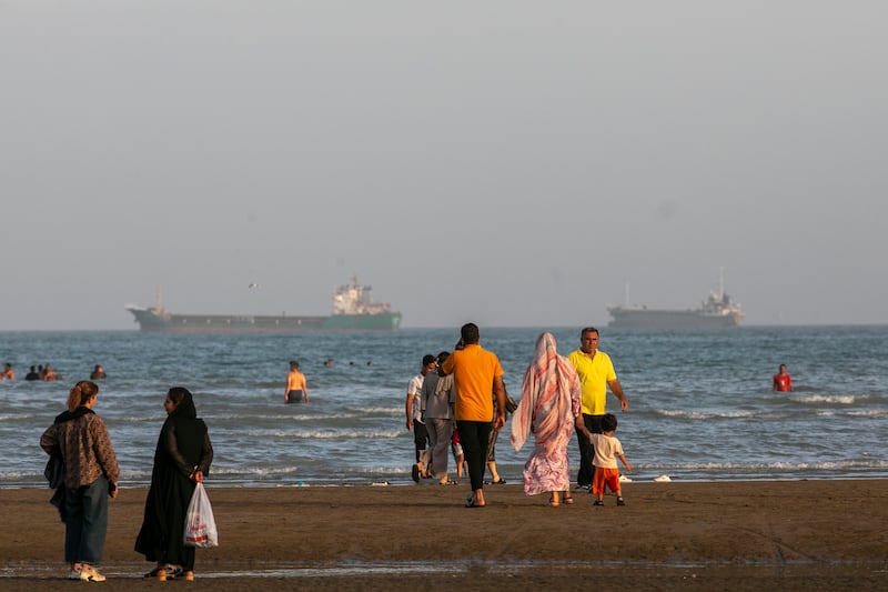BANDAR ABBAS, IRAN - MAY 15: People are seen along the coast of the Persian Gulf, while Iranian and foreign cargo vessels wait in the background for clearance to pass through the Strait of Hormuz on May 15, 2026 in Bandar Abbas, Iran. Since the outbreak of the US-Israeli war against Iran, forcing the closure of the Strait of Hormuz, global shipping routes have been severely impacted with little progress being made in the negotiations between Iran and the United States. Soaring shipping costs, lengthening delivery times and less efficient routes have seen increased pressure on energy markets and supply chains worldwide. (Photo by Majid Saeedi/Getty Images)