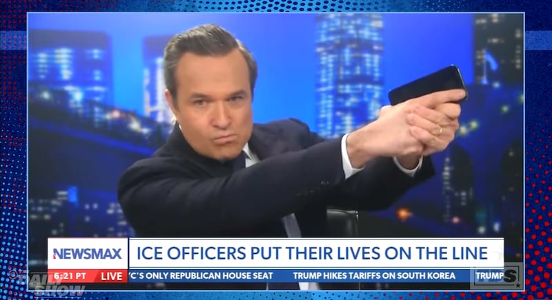 Greg Kelly holding his phone like a gun on Newsmax, clip shown on The Daily Show.