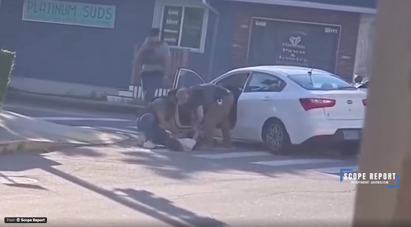 Two men in ICE vests drag a man out of white Kia Ceed