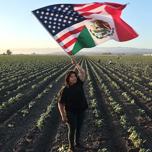 CAMARILLO, CALIFORNIA - JULY 10: Community member Ana waves an American-Mexican flag in a show of support for detainees near federal agents blocking protestors during an ICE immigration raid at a nearby licensed cannabis farm on July 10, 2025 near Camarillo, California. Ana said she knows some of those detained and their families. Protestors stood off with federal agents for hours outside the farm in the farmworker community in Ventura County. A Los Angeles federal judge is set to rule Friday on a temporary restraining order which would restrict area immigration enforcement operations. (Photo by Mario Tama/Getty Images)