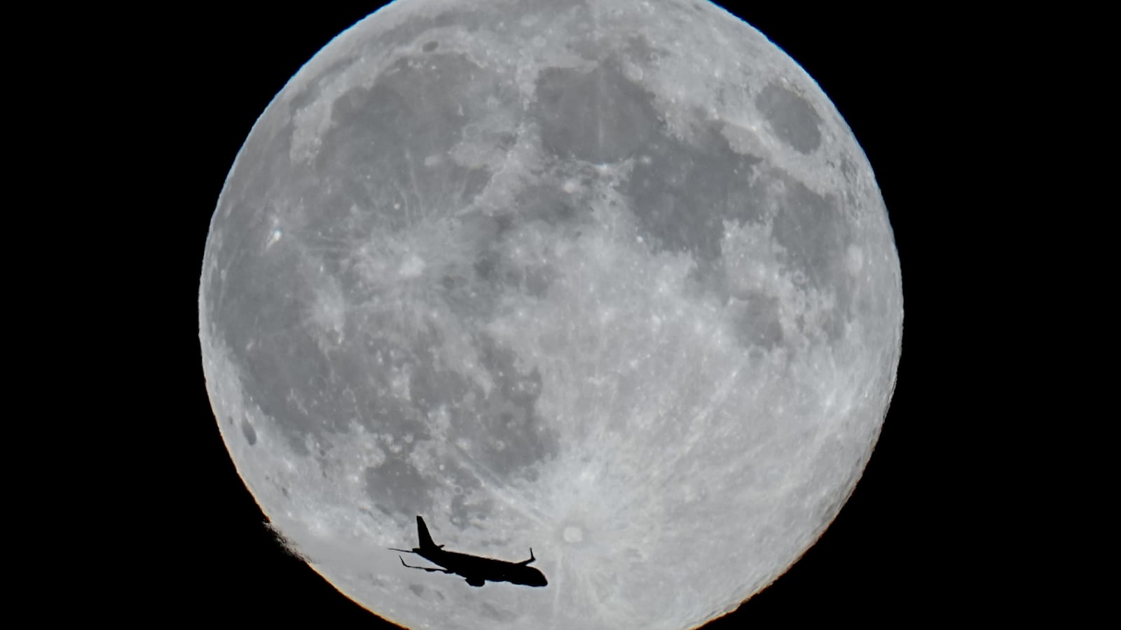An airplane flies past the full moon over Berlin