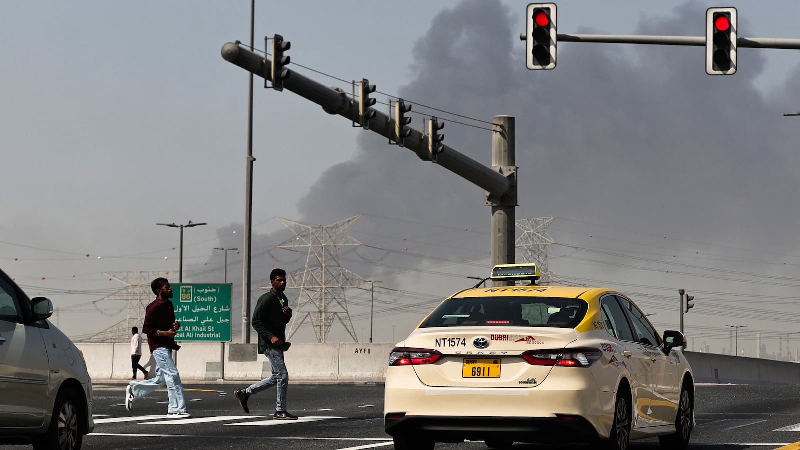People cross a street as smoke rises from the site of a reported Iranian strike in Dubai on March 1, 2026