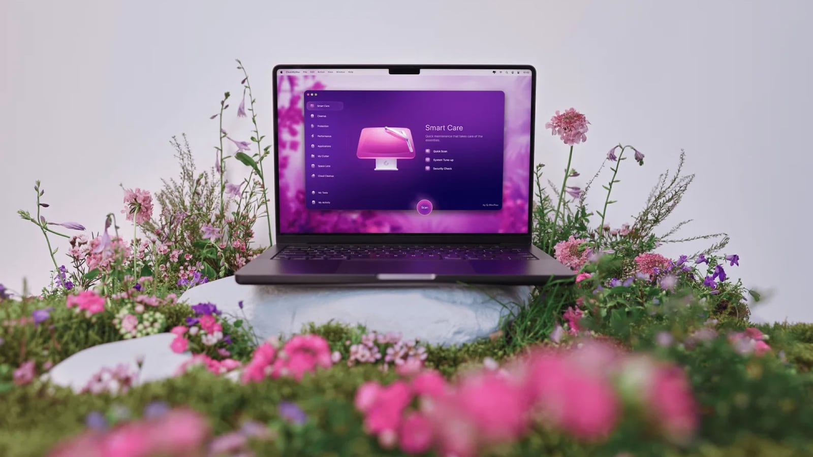 A Mac sitting on a rock in a field of flowers. The screen is showing the CleanMyMac software.