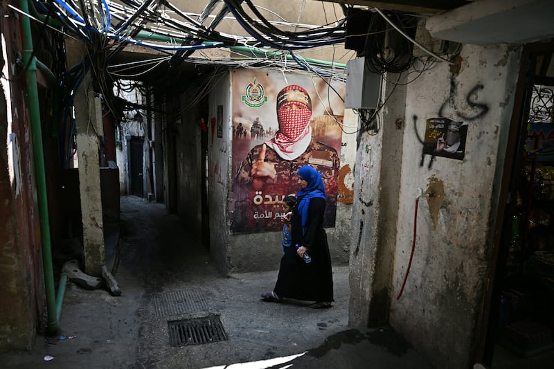 A woman walks past a wall poster depicting Abu Obaida