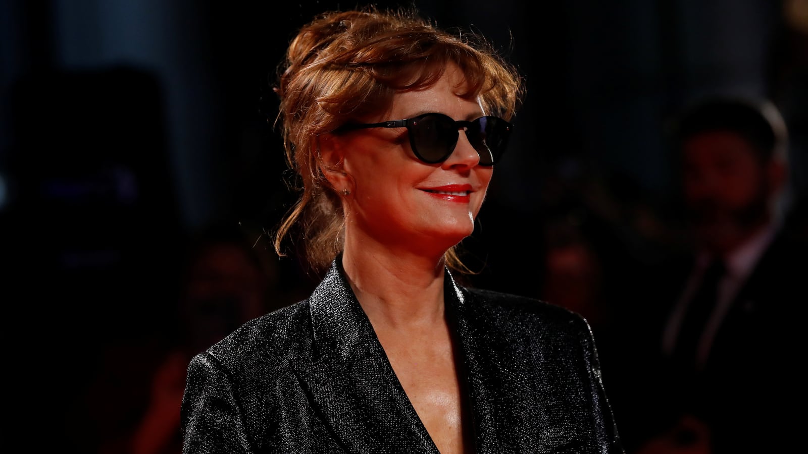 Susan Sarandon, wearing a black dress and glasses, smiles at a film festival.