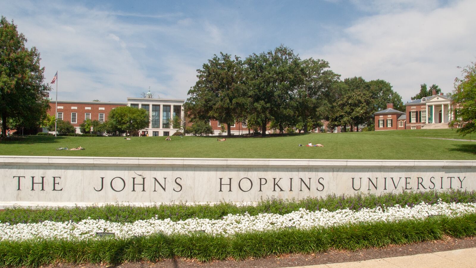Close-up of sign reading The Johns Hopkins University with MSE Library and Homewood House museum in the background