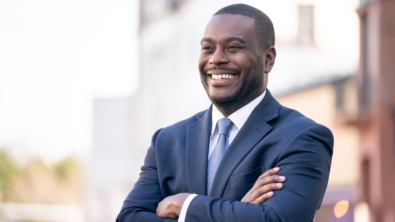 Gabe Amo smiles in a headshot with his arms crossed.