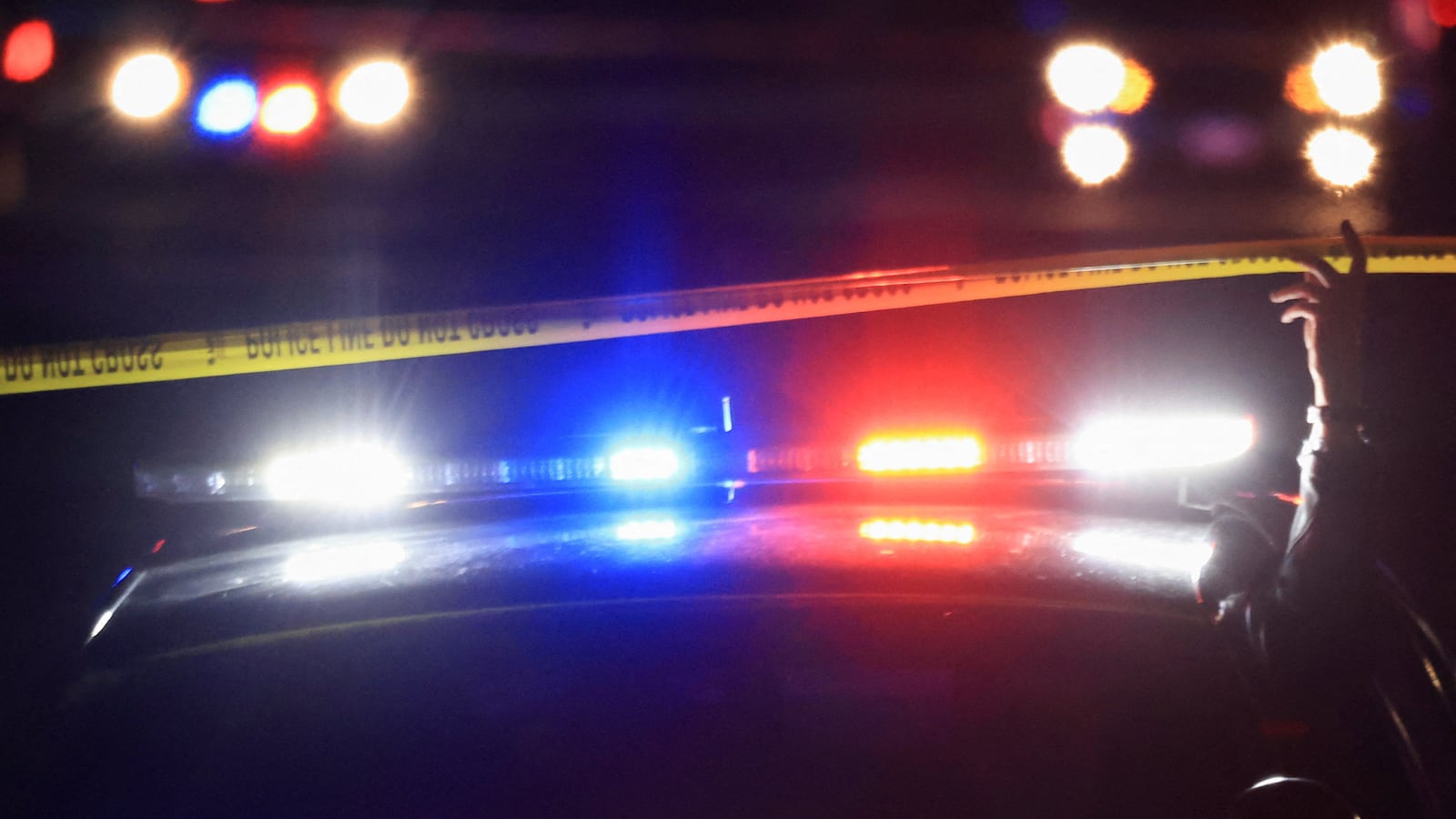 A police cruiser drives under yellow police tape at night.