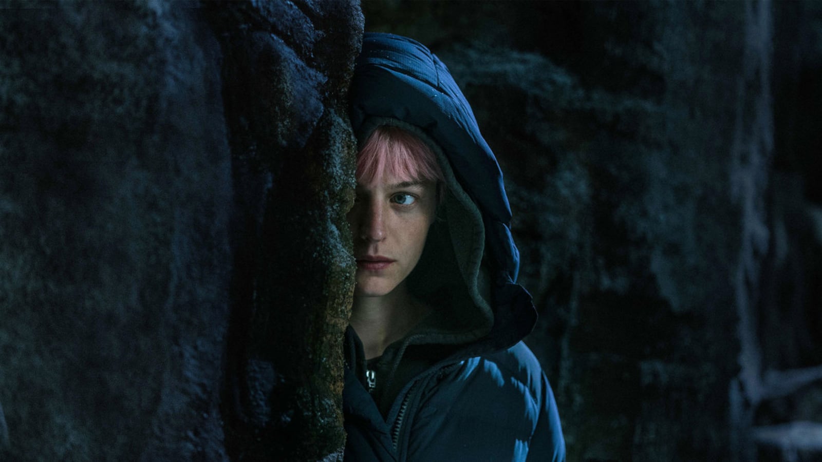 Emma Corrin peering out behind a wall in a still from ‘Murder at the End of the World’