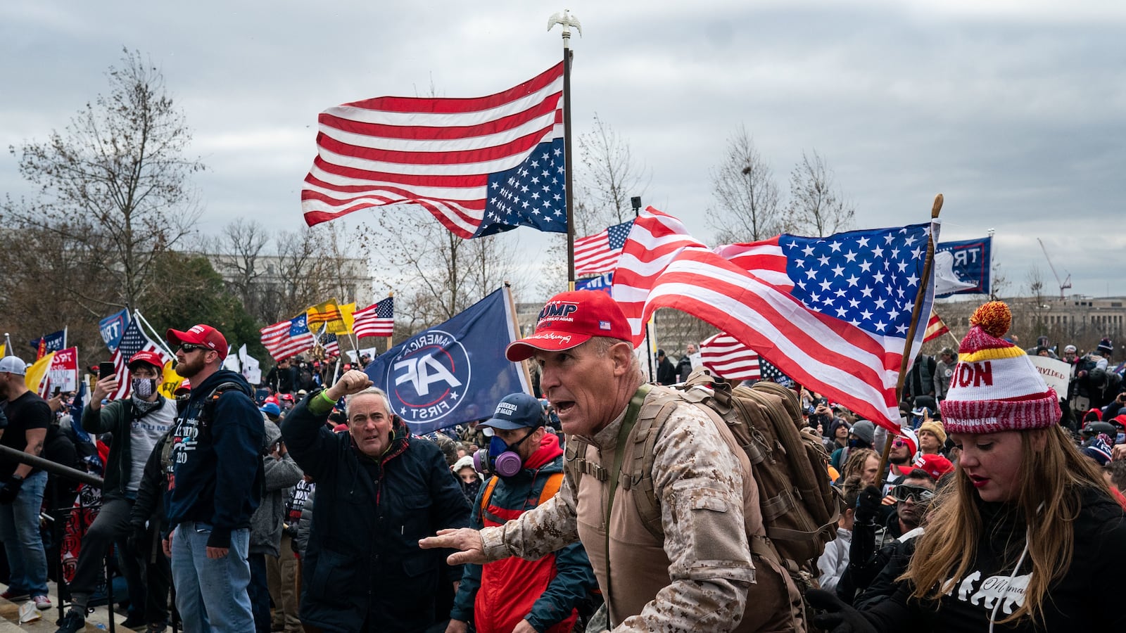 Ray Epps, in the red Trump hat, center, gestures to a line of law enforcement officers, as people gather on the West Front of the U.S. Capito
