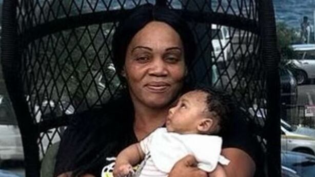 Neville Hewitt stands next to his mother, Deon Jones, who is holding his son.