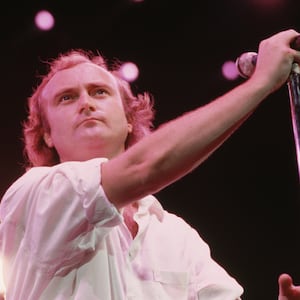 Phil Collins, holding a microphone on stage during a concert