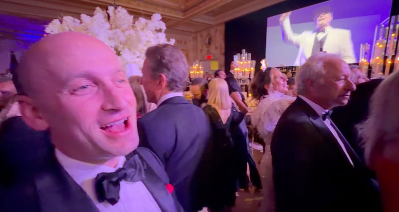 Stephen Miller finally cracks a smile, as Vanilla Ice can be seen on the screen in the background.