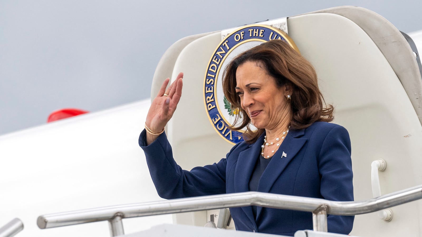 Kamala Harris waves as she steps off a plane.