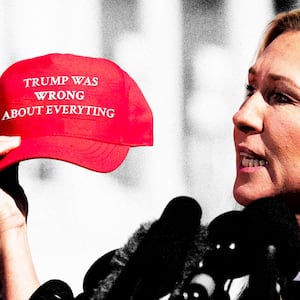 Marjorie Taylor Greene holding a red hat that says "Trump was wrong about everything"